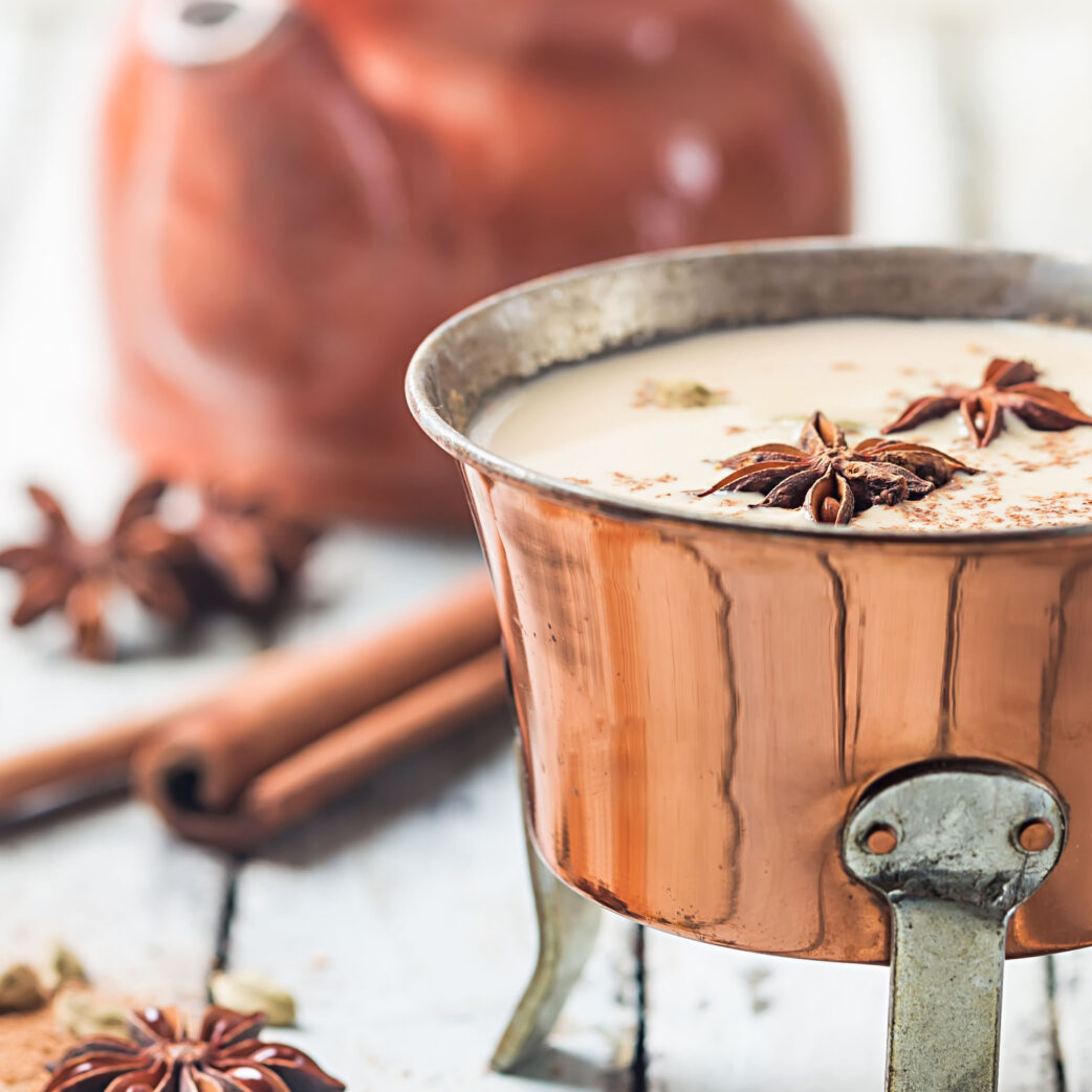 Indian masala chai tea, spiced tea with milk in a copper pot over white wooden background